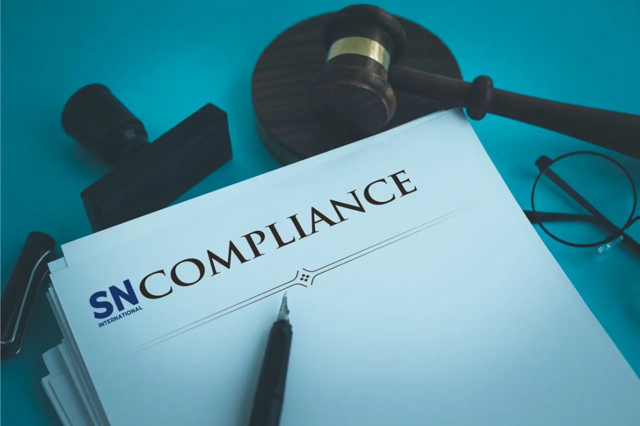 A document labeled "Compliance" with the SN International logo, accompanied by a pen, a gavel, and a pair of glasses on a blue background.