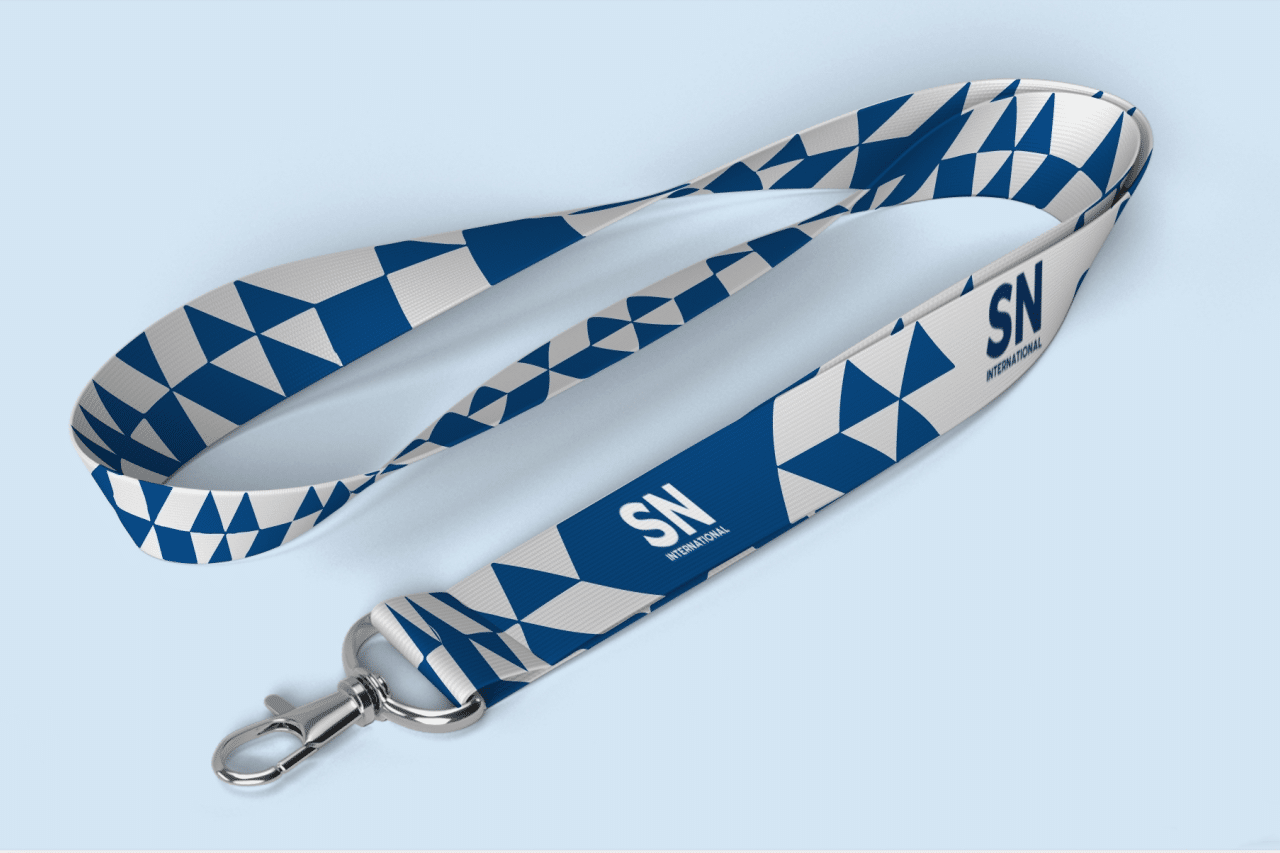 A custom branded lanyard featuring a blue and white geometric pattern with the SN INTERNATIONAL logo prominently displayed. The lanyard includes a metal clip attachment, ideal for use at trade shows and events.